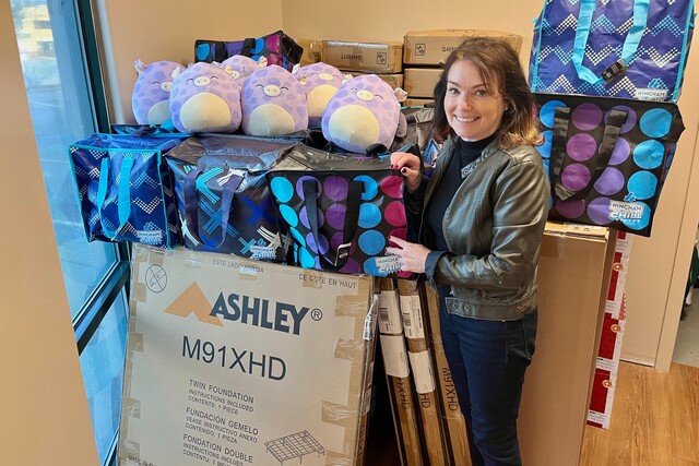 Executive Director Helen Brownrigg standing beside bed kits donated by Ashley Furniture for families who lost their homes to the fires in the Okanagan summer 2023